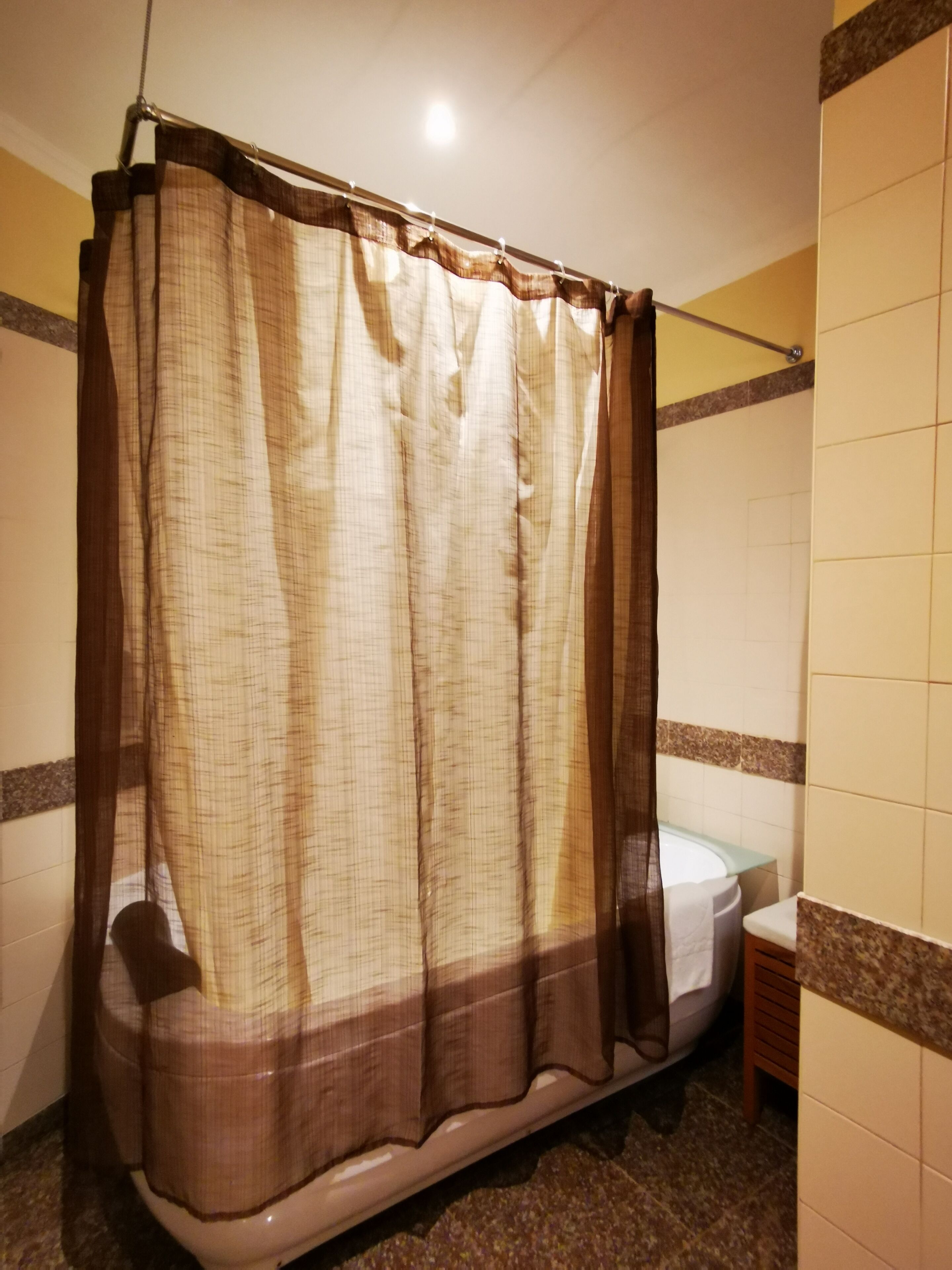 Baño con cortina de ducha, bañera y un taburete de madera.