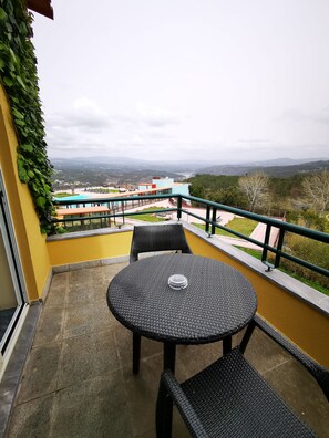 Un balcón con una mesa redonda y dos sillas, con vistas a un paisaje urbano y montañas.