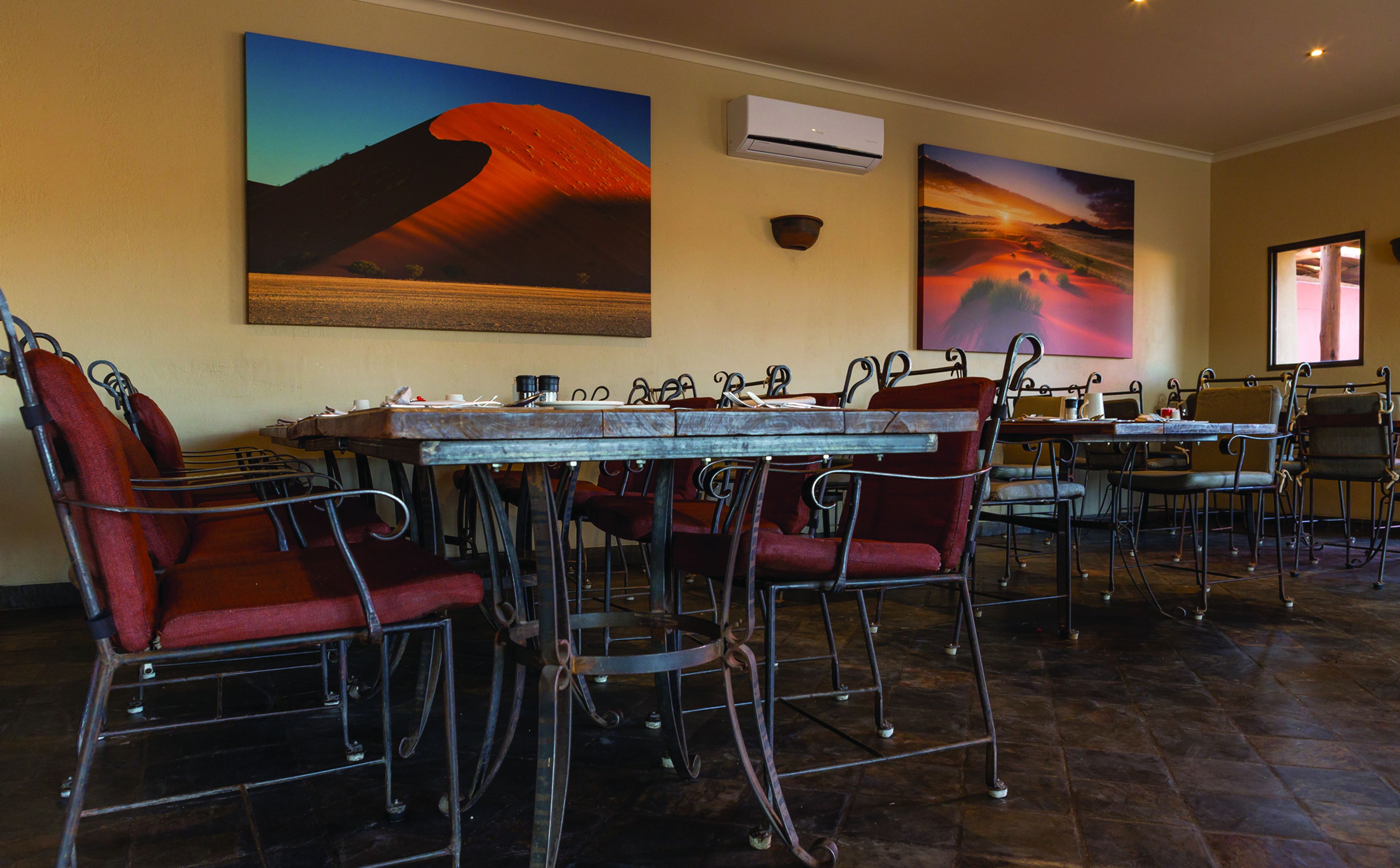 A dining area with a long table, red upholstered chairs, and two large desert landscape paintings on the wall.