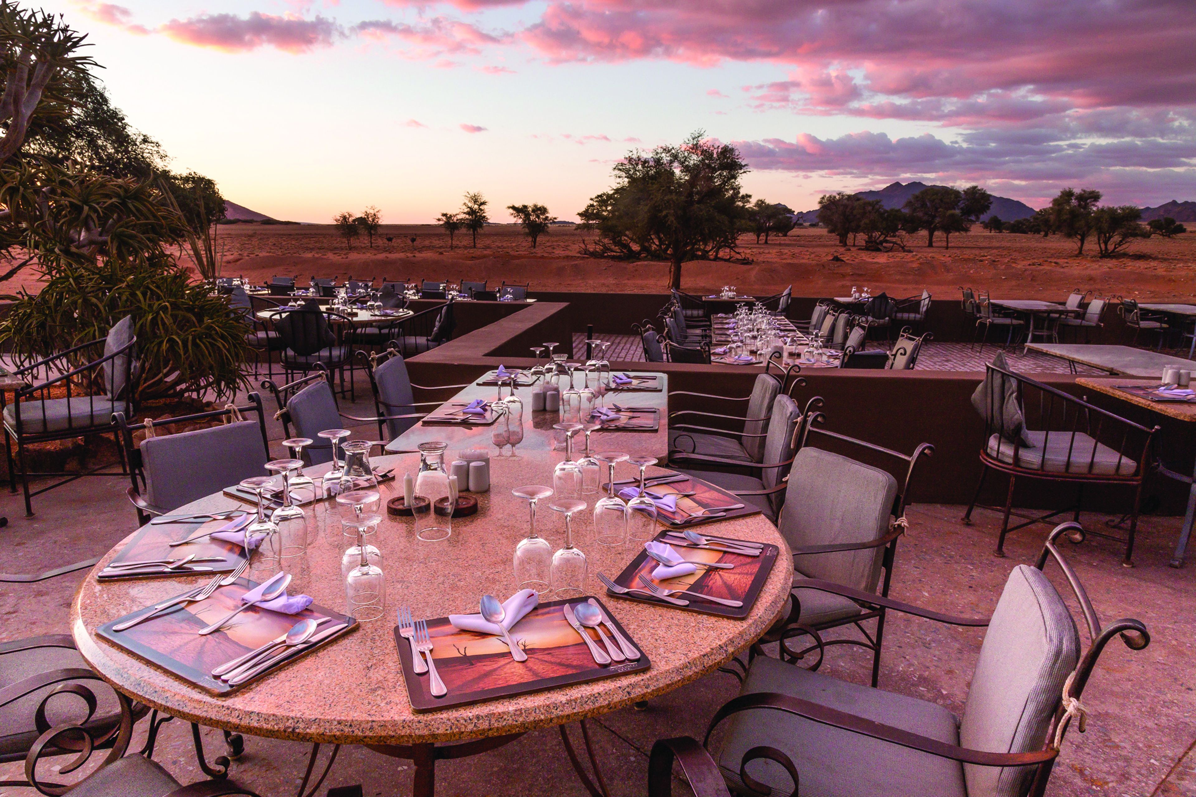 Un restaurant doté d’une terrasse, avec des tables dressées et ornées de couverts et de verres, et un paysage désertique en arrière-plan.