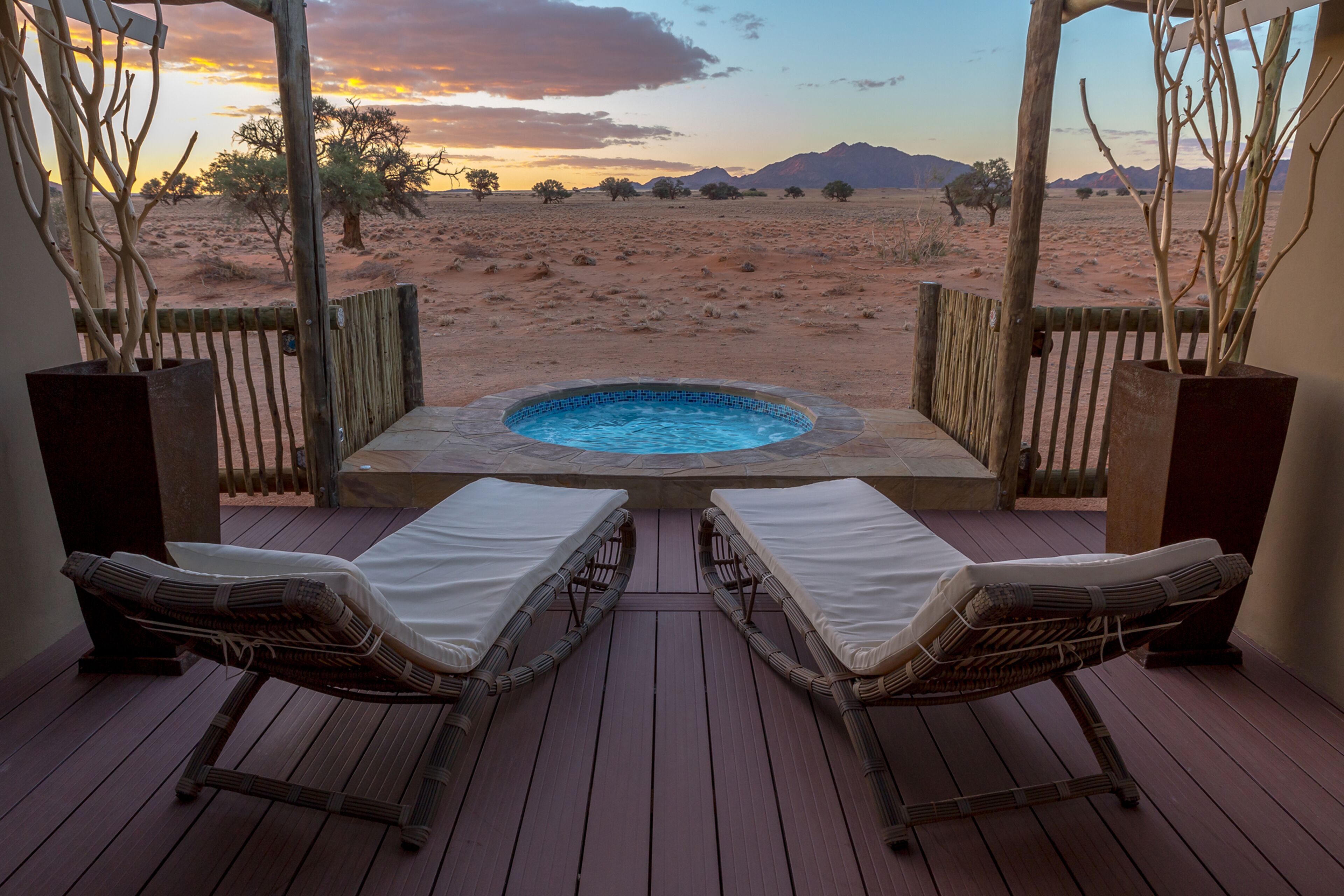A wooden deck with two wicker lounge chairs facing a hot tub and a desert landscape.