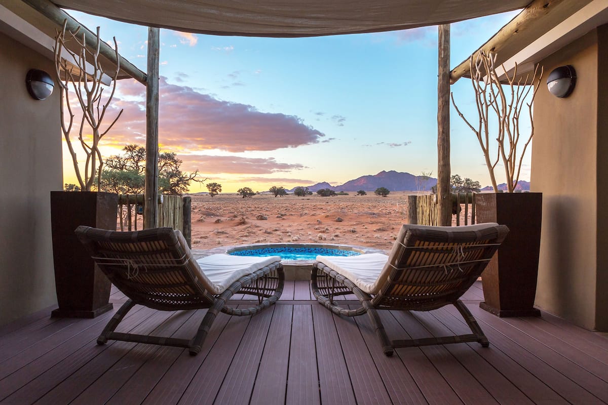 A deck with two wicker lounge chairs facing a pool and a desert landscape.