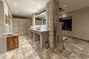 A modern bathroom with a stone wall, a wooden vanity, a large mirror, and a bathtub.