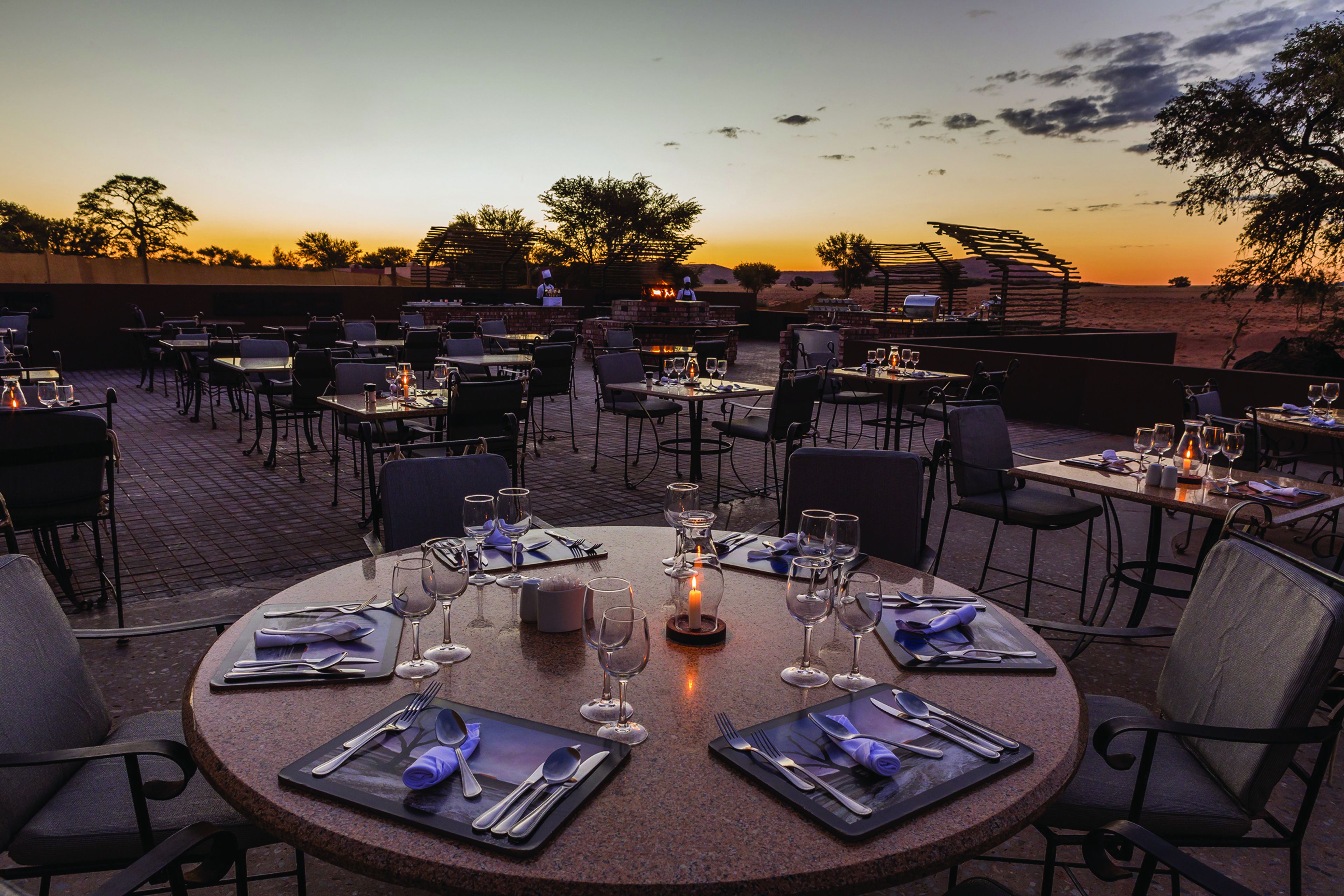 An outdoor dining area with round tables set for two, each with cutlery and wine glasses.