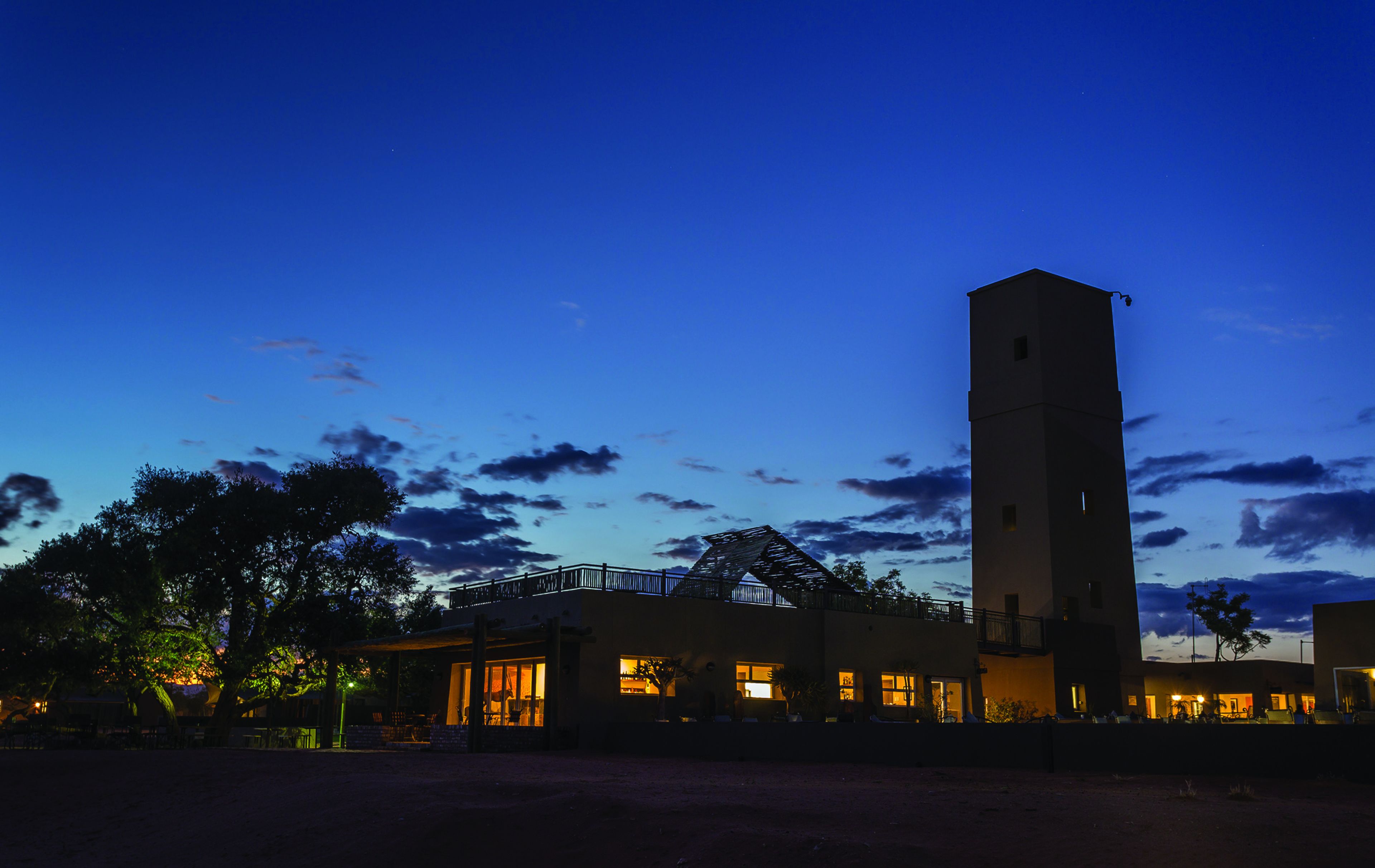 Un edificio con una torre destacada, un espacio al aire libre cubierto con asientos y una entrada bien iluminada.
