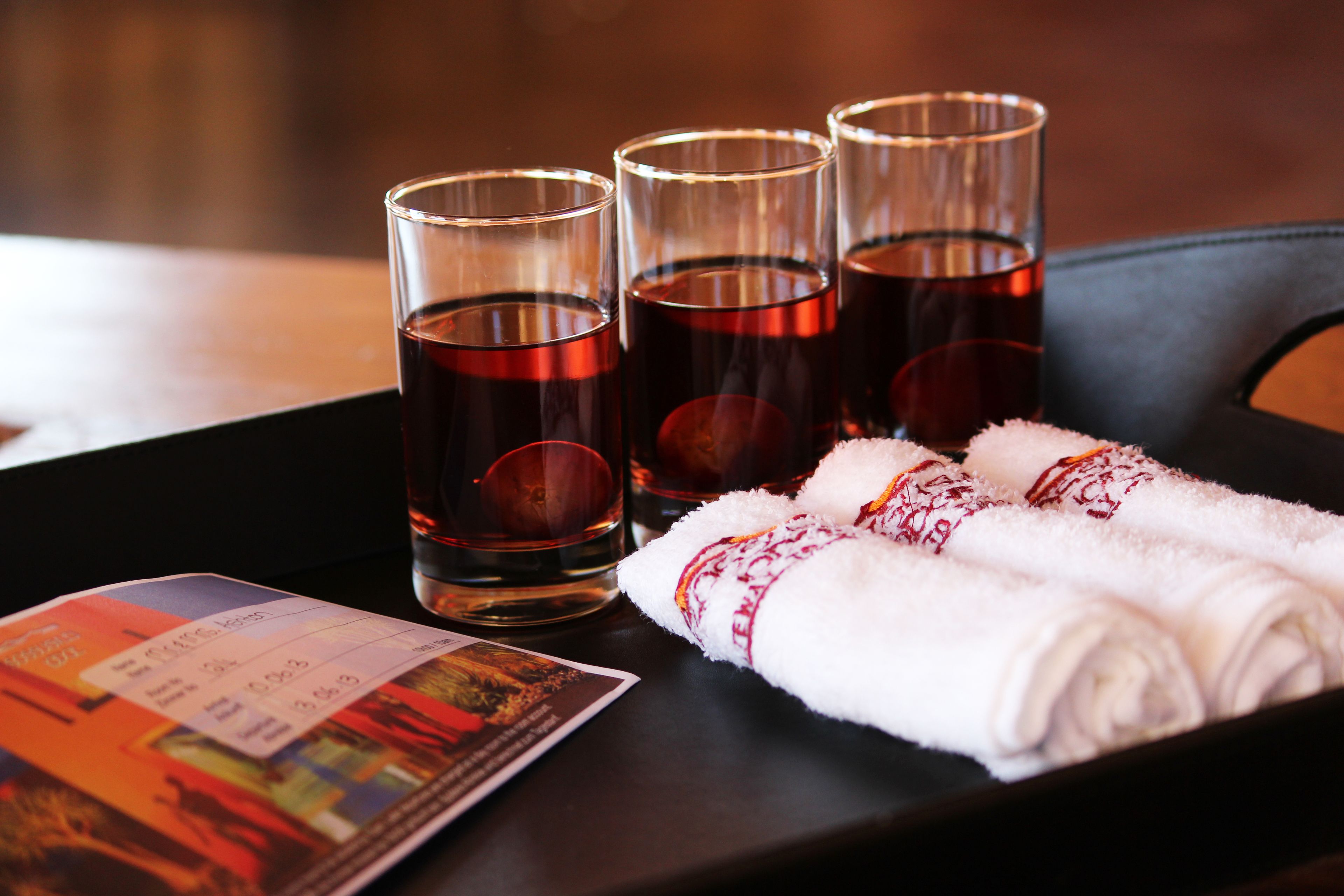 A tray with three glasses of dark liquid, a folded white towel with red embroidery, and a printed item.