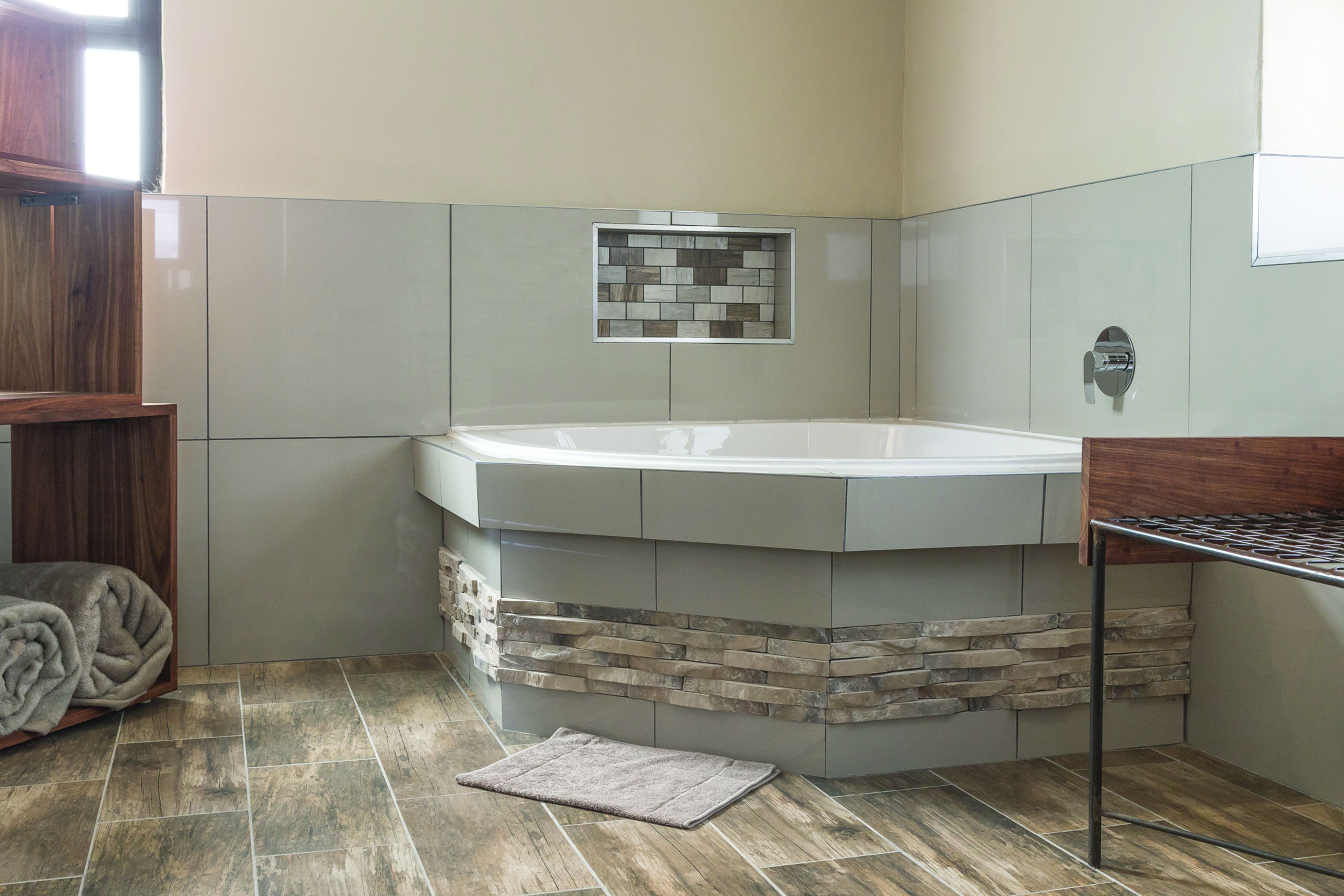 A bathroom with a stone accent wall, a bathtub, and a wooden bench.