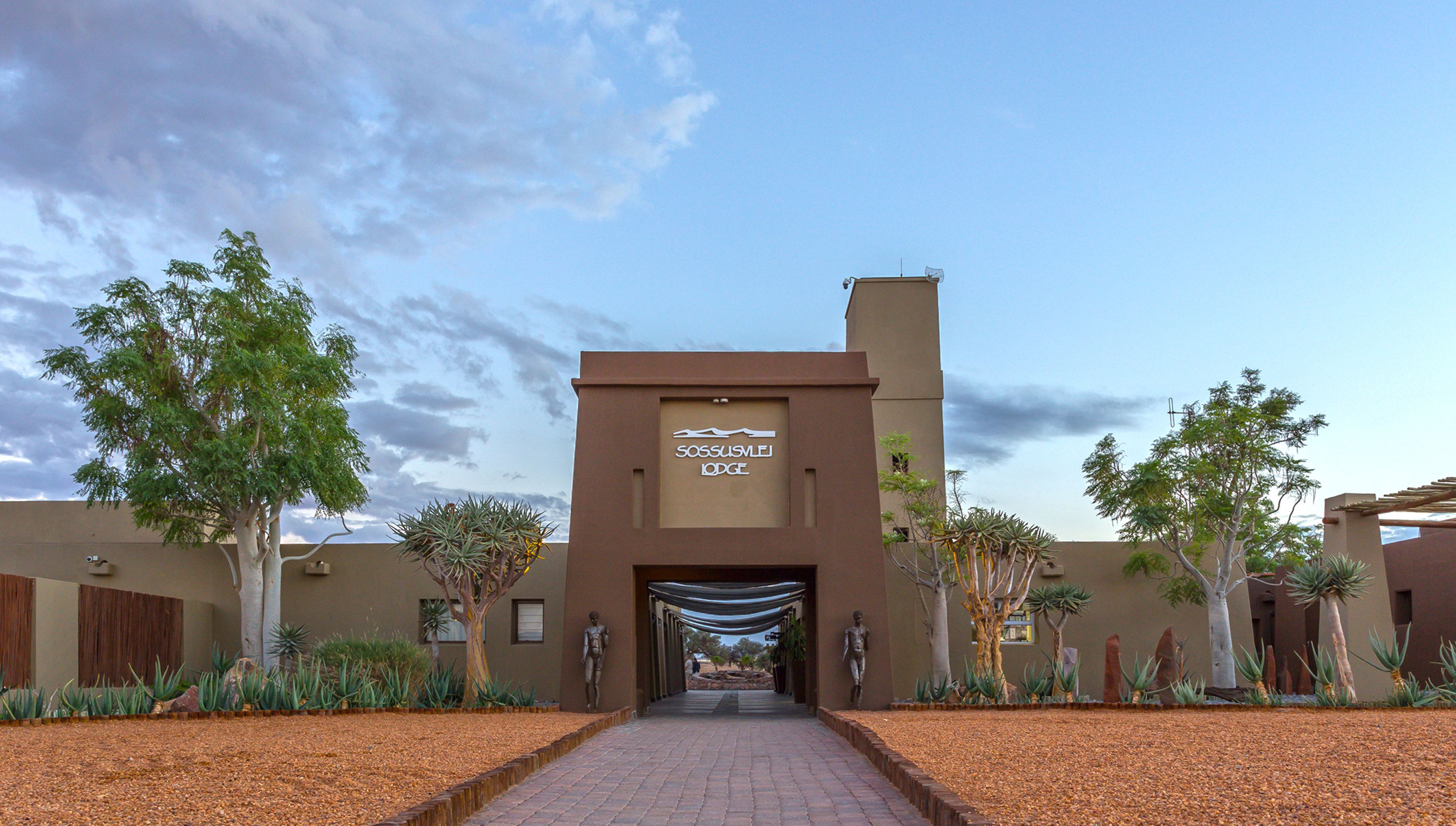 L'entrée du Sossusvlei Lodge est clairement indiquée par un chemin menant au bâtiment, lequel est entouré d'espaces aménagés avec différentes espèces de plantes.