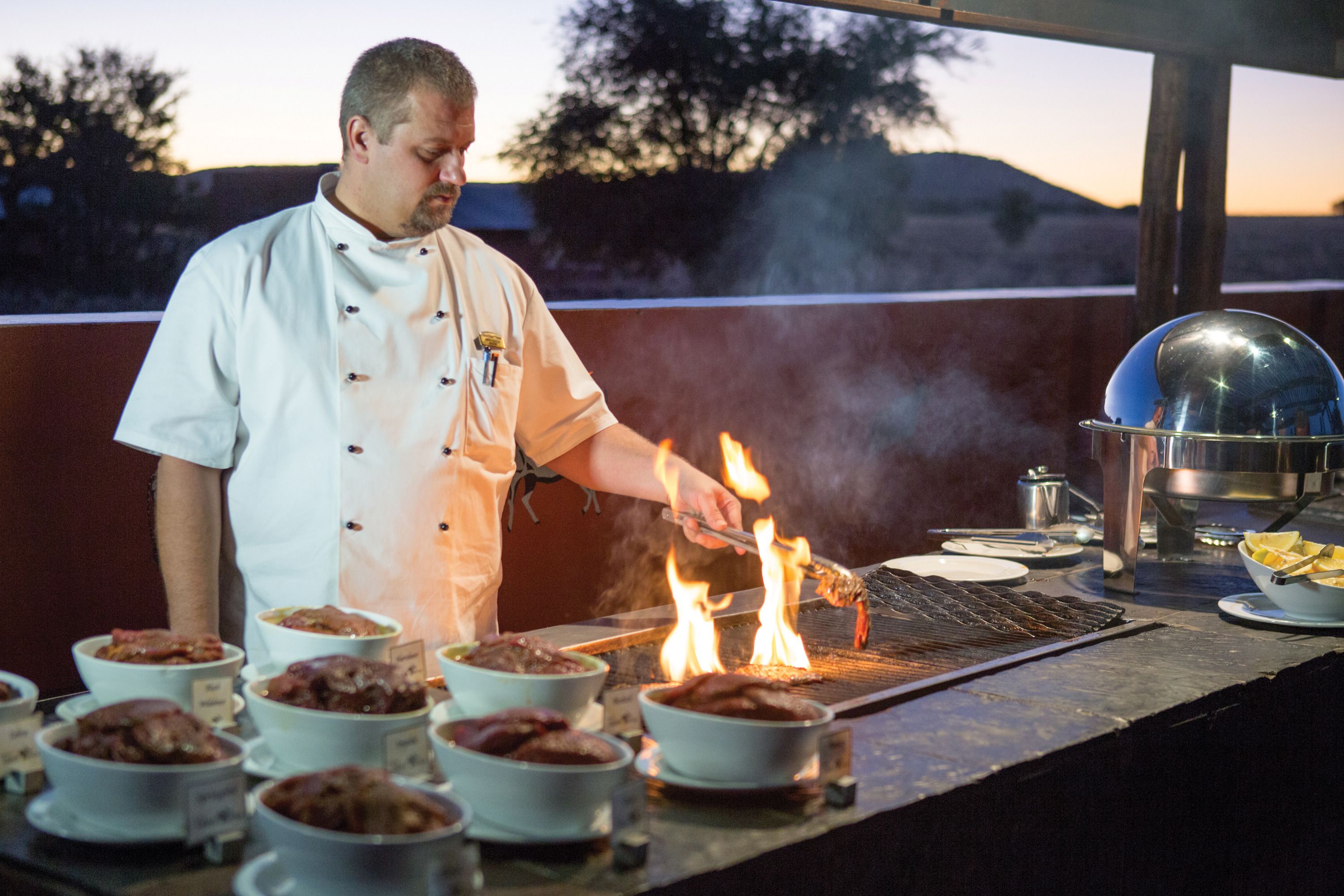 A chef cooking outdoors with a grill and various dishes in bowls.