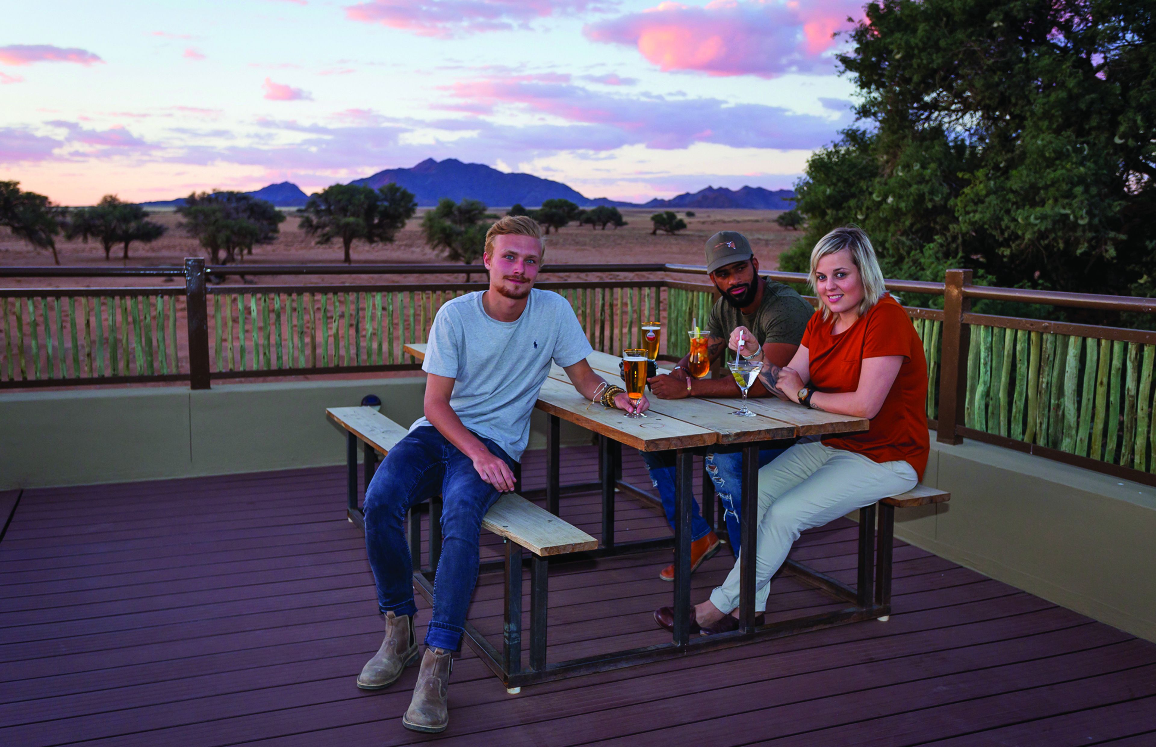 A wooden deck with a table and benches, overlooking a landscape with trees and mountains.