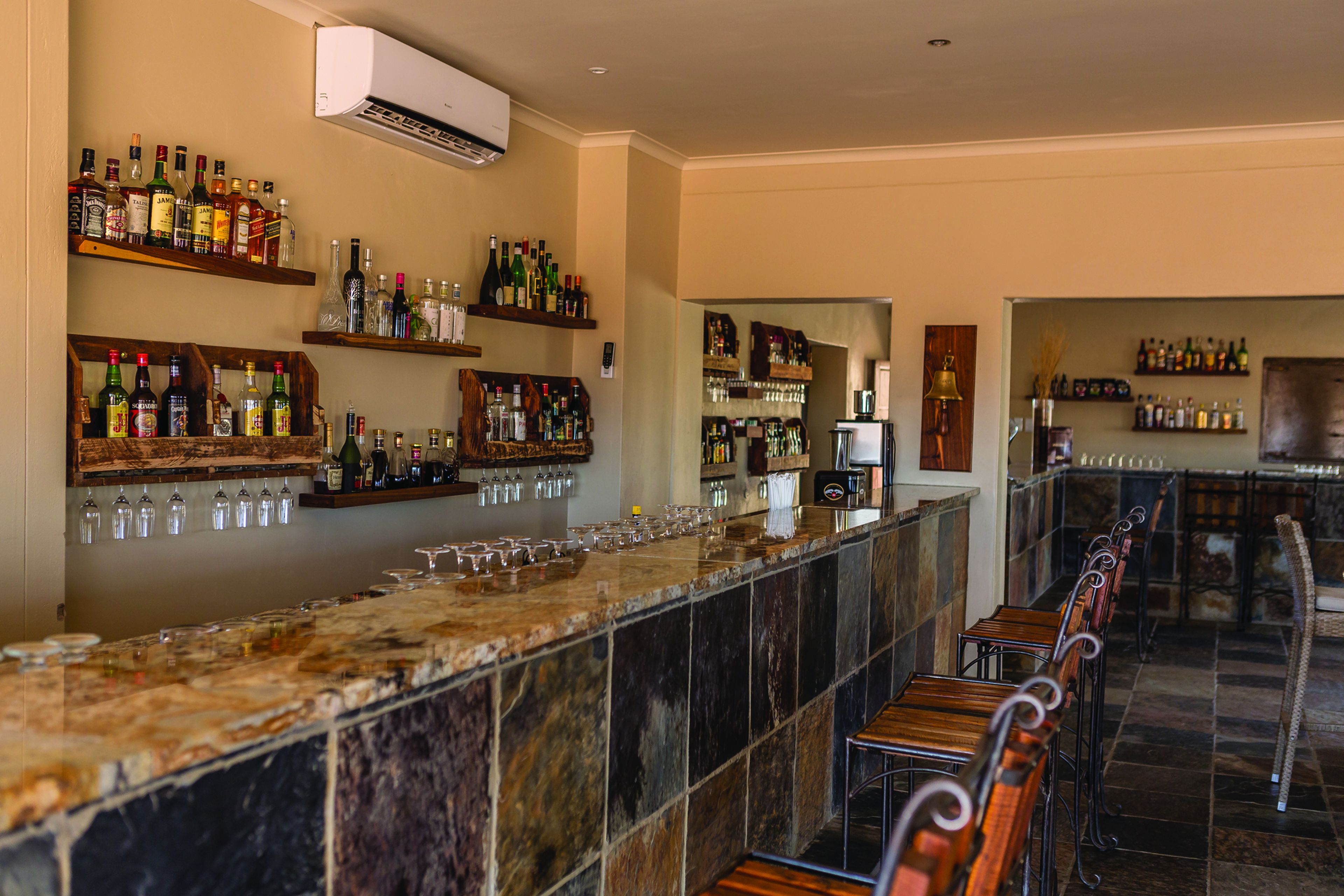 Eine Bar mit einer langen Theke, Regalen voller Flaschen, Gläsern und einer Kaffeemaschine.