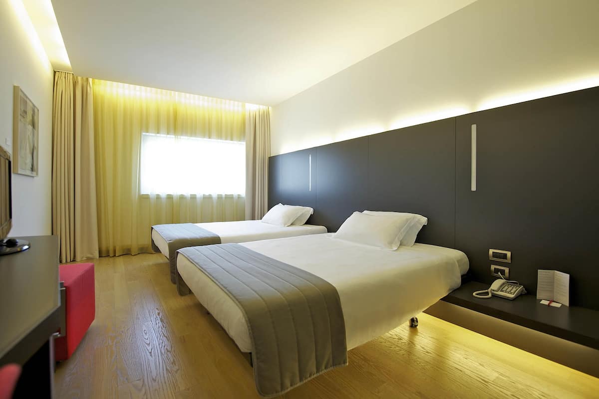 A hotel room with two beds, a desk, a telephone, and a window with curtains.