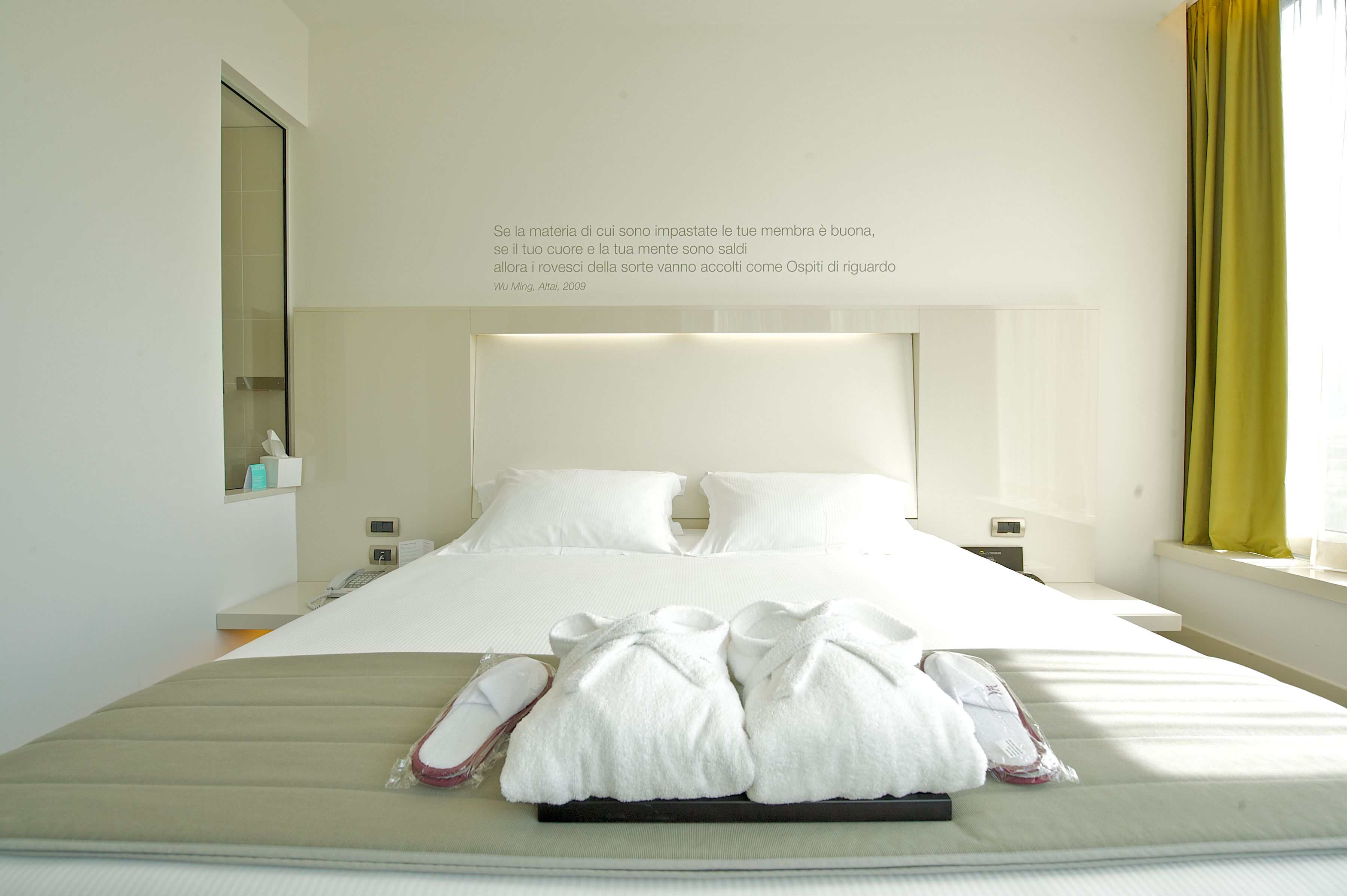 Una habitación de hotel con una cama grande, una mesita de noche, un espejo y una ventana con cortinas.