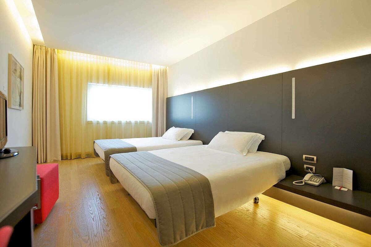 A hotel room with two beds, a desk, a phone, and a window with curtains.