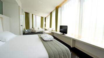 A hotel room with a large bed, a TV on a bedside table, a sofa, and a desk.