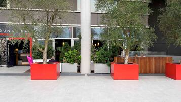 Un edificio moderno con área de recepción, asientos exteriores y plantas en macetas.