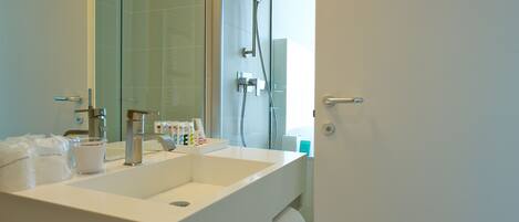 Un baño moderno con un lavabo blanco grande, una cabina de ducha de vidrio y una toalla colgada en un perchero.