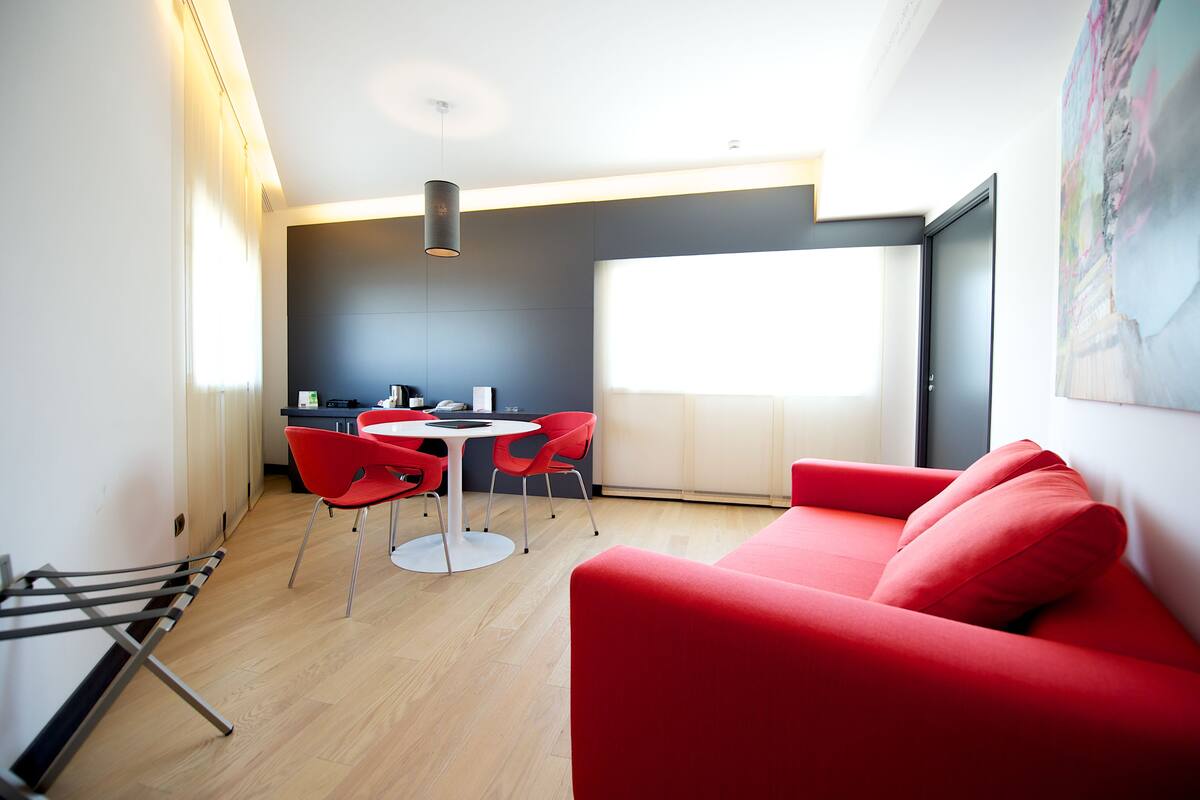 A modern living space with a red sofa, a dining area with a table and chairs, and a large window providing natural light.