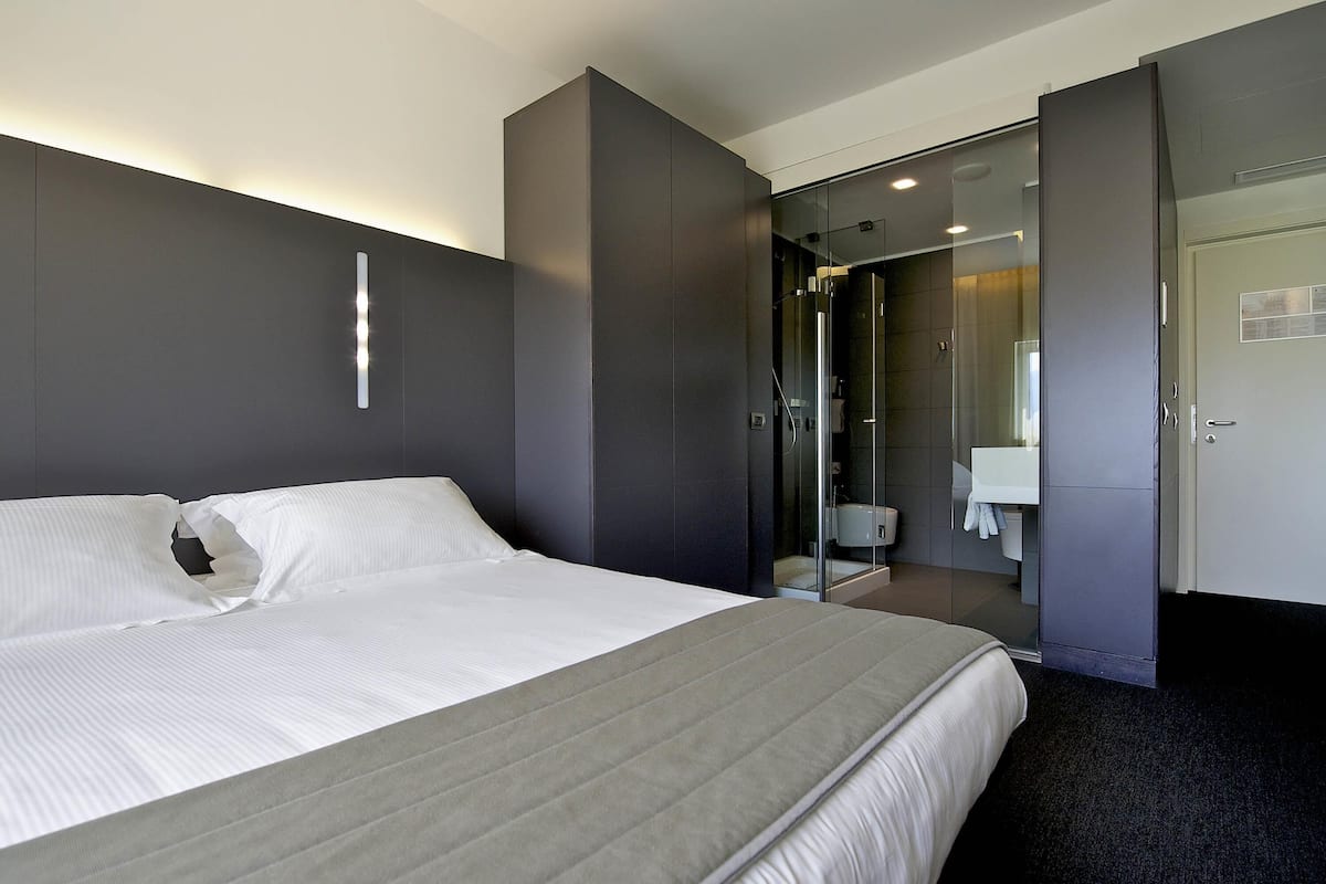 A modern hotel room with a large bed, a walk-in closet, and a bathroom with a glass shower enclosure.
