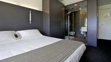 A modern hotel room with a large bed, a walk-in closet, and a bathroom with a glass shower enclosure.