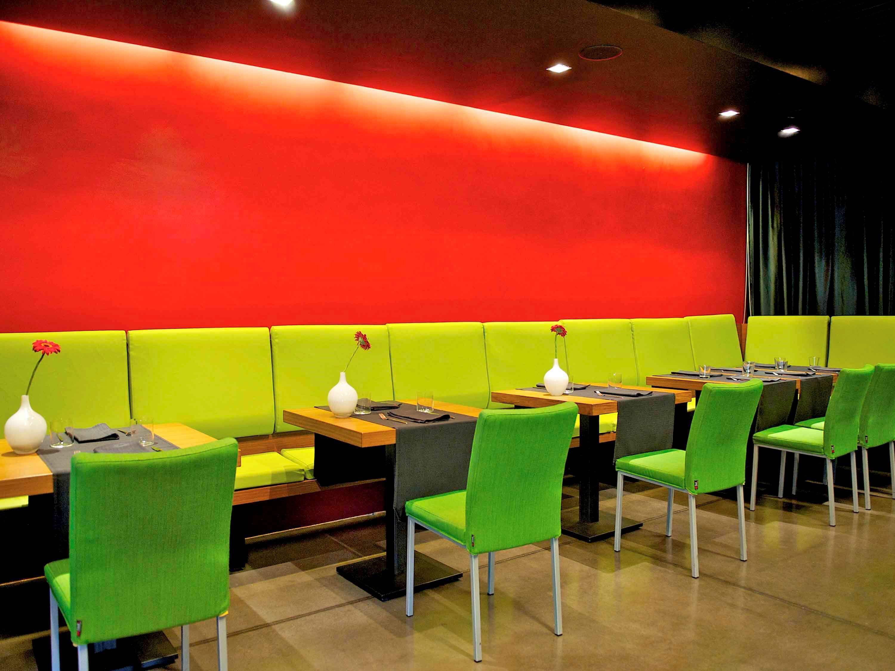 A restaurant with green booths and chairs, tables with menus, and vases with flowers.