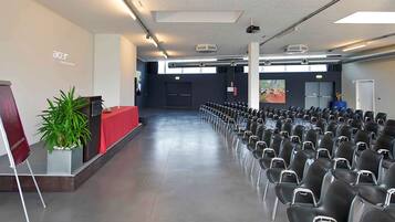 Une salle de conférence avec des rangées de chaises, un pupitre et un grand écran.