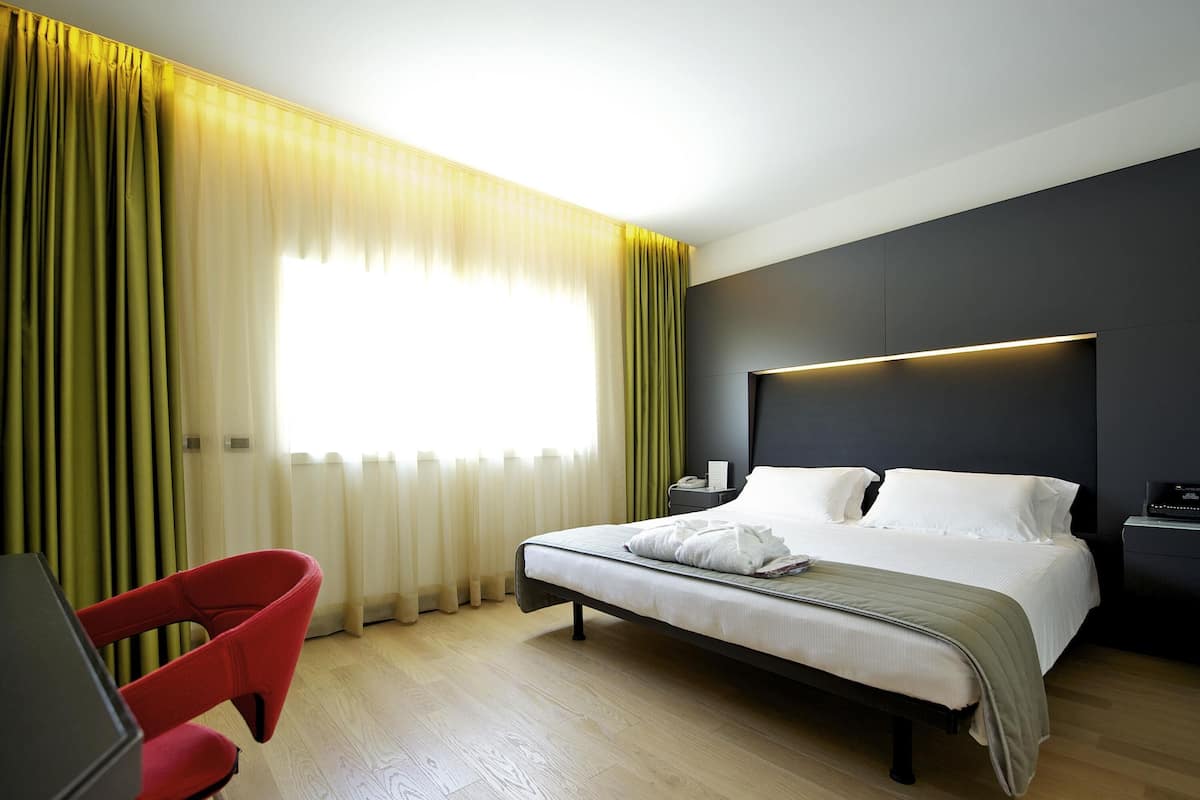 A hotel room with a bed, a desk, a chair, and a window with curtains.