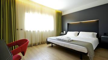 A hotel room with a bed, a desk, a chair, and a window with curtains.