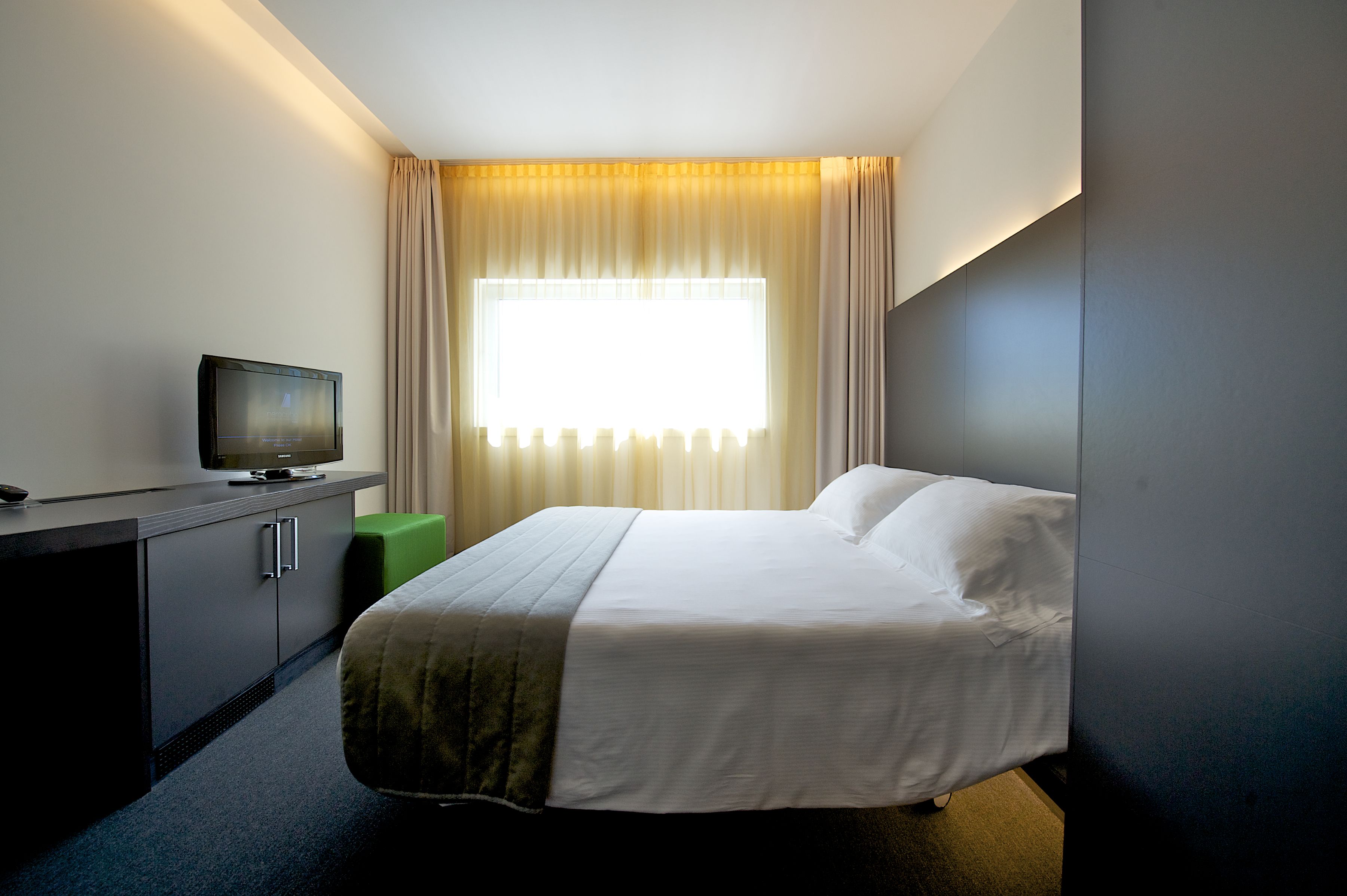 A hotel room with a bed, a television on a desk, and a window with curtains.