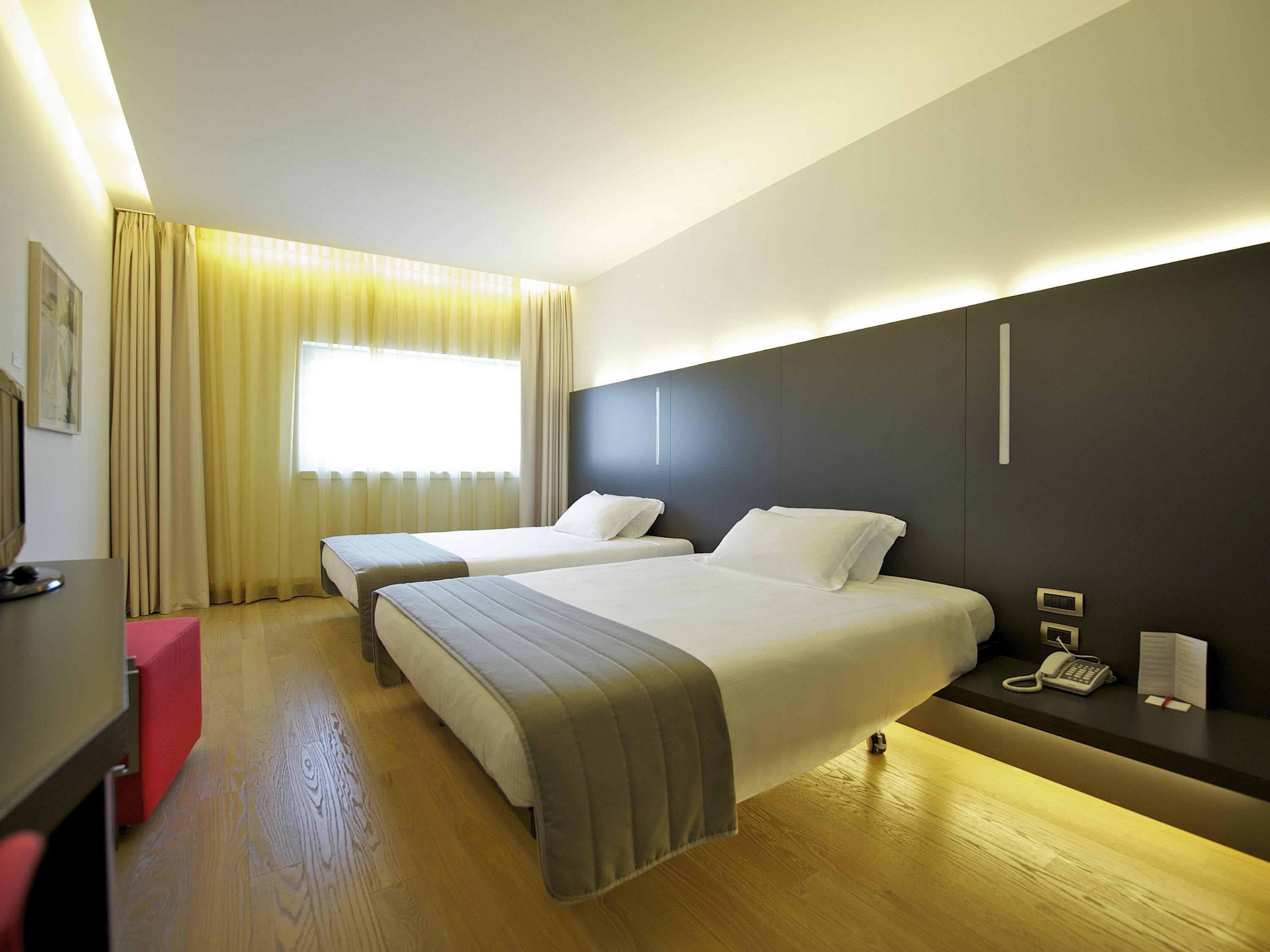 A hotel room with two beds, a desk, a telephone, and a window with curtains.