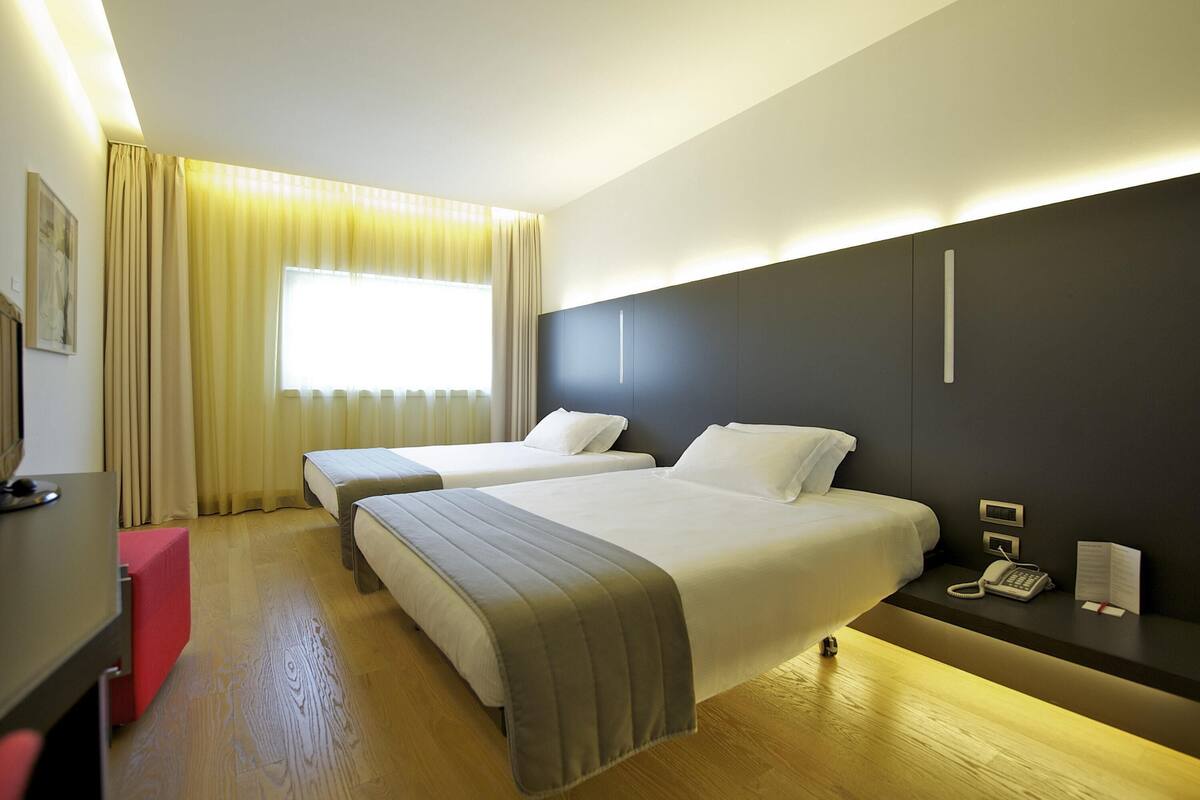 A hotel room with two beds, a desk, a telephone, and a window with curtains.
