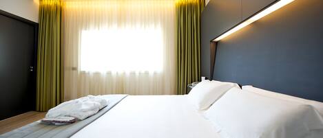 Una habitación de hotel con una cama, una mesita de noche y un ventanal con cortinas.