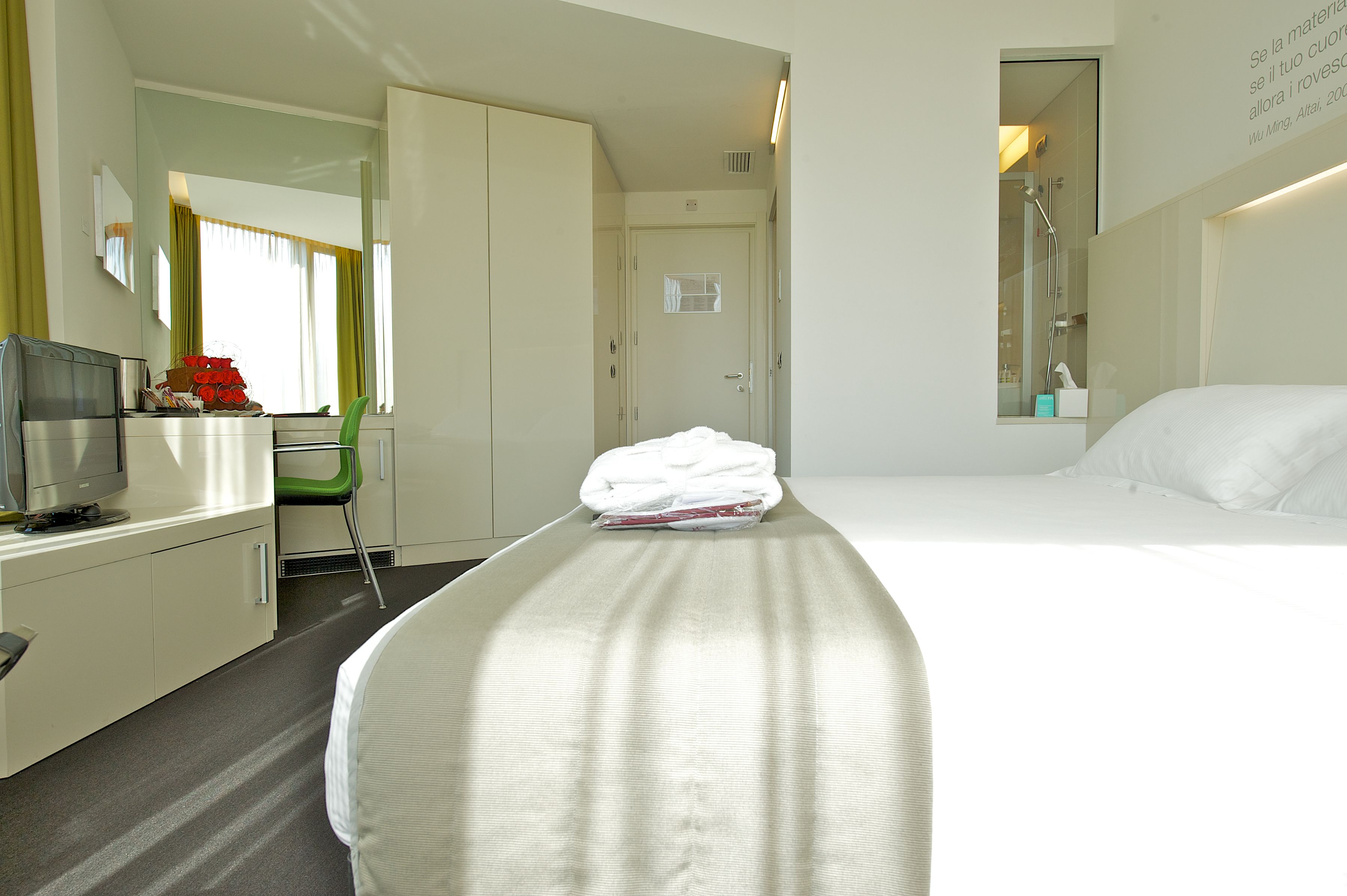 Hotelkamer met een bed, bureau, stoel, televisie en een badkamer, zichtbaar door een geopende deur.
