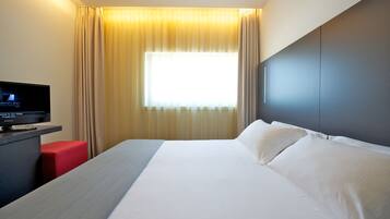 Een hotelkamer met een groot bed, een flatscreen televisie, een rode stoel en een raam met gordijnen.