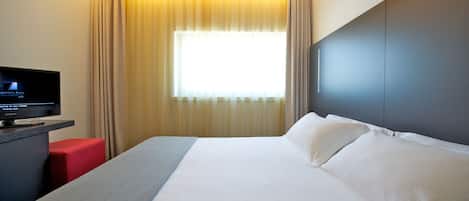 Habitación de hotel con una cama grande, un televisor de pantalla plana, una silla roja y un ventanal con cortinas.
