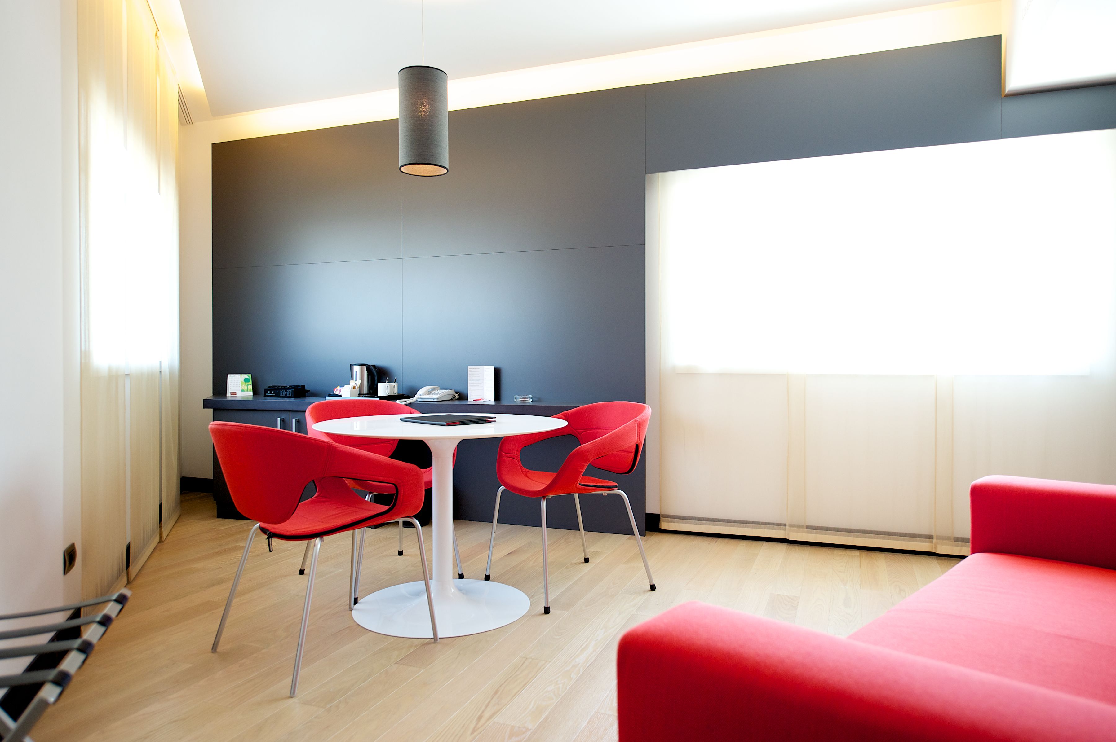 A modern room with a dining table and chairs, a kitchen area, and a large window providing natural light.