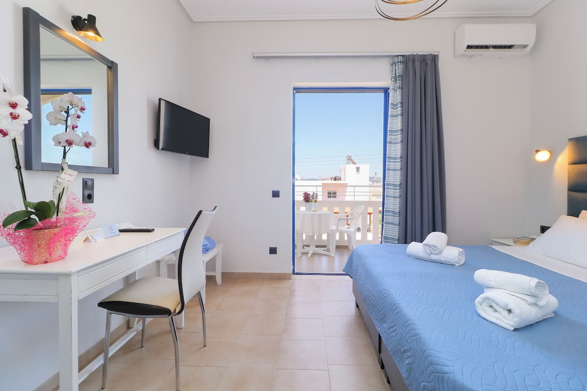 Habitación de hotel con escritorio, silla, cama y balcón.