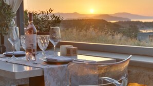 A table set for dining with a bottle of wine, glasses, and plates, overlooking a scenic sunset view. - Alexis Hotel (Chania)
