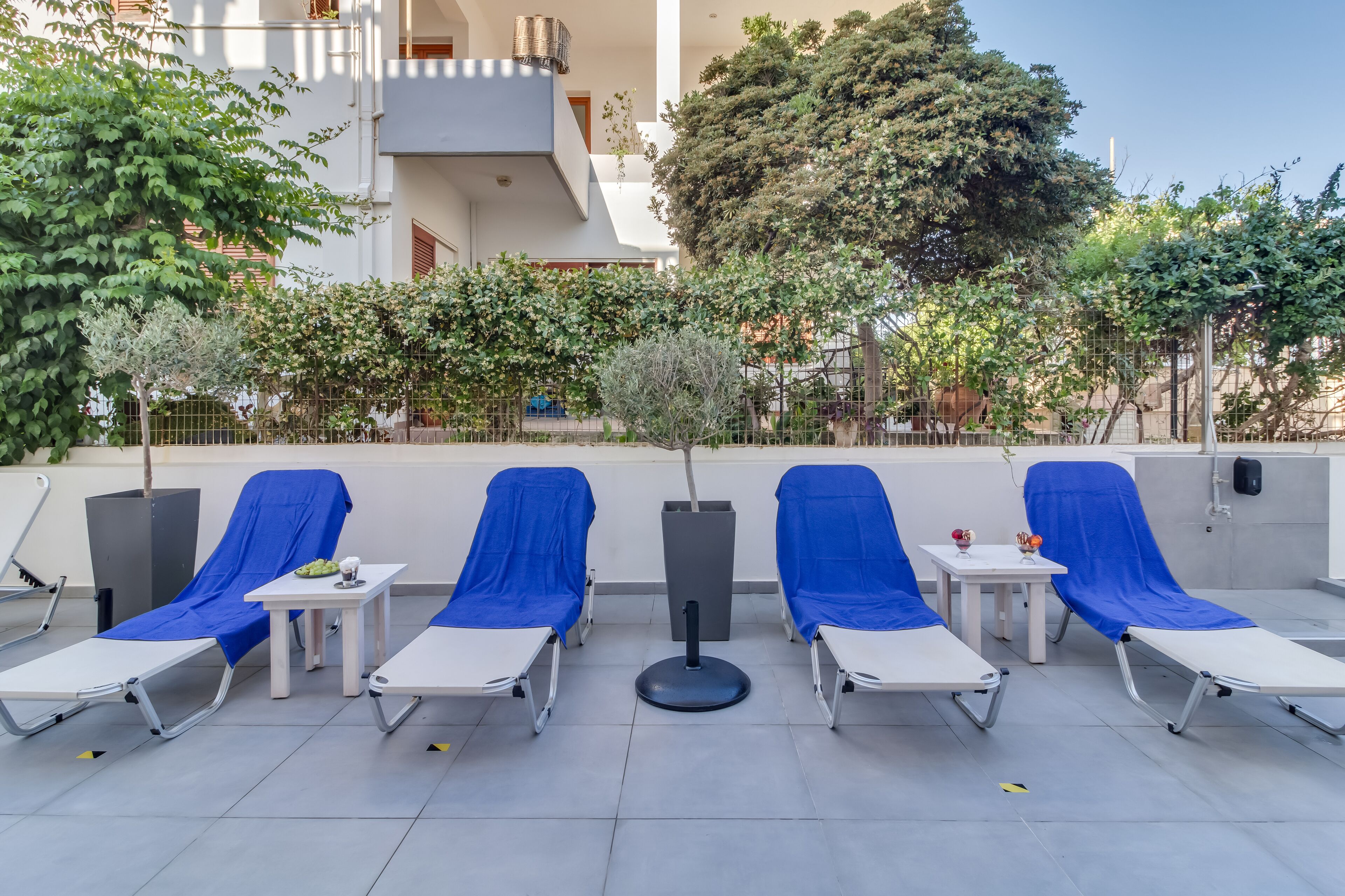 A rooftop lounge area with sun loungers, small tables, and potted plants.