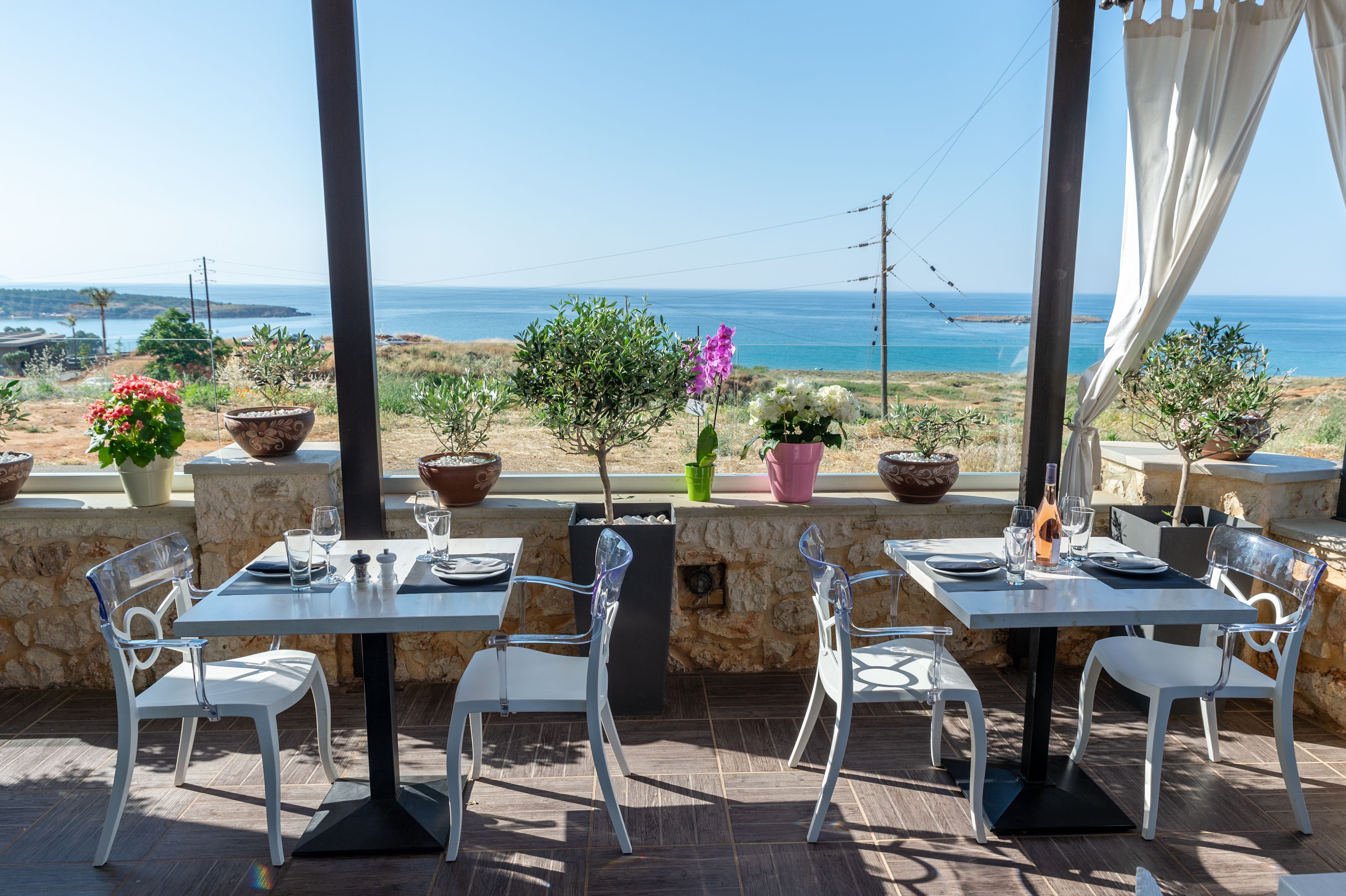 An outdoor dining area with tables and chairs, potted plants, and a view of the ocean.