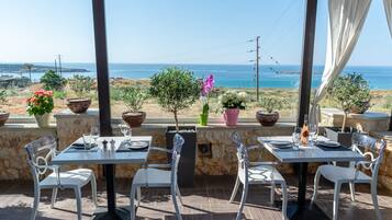 An outdoor dining area with tables and chairs, potted plants, and a view of the ocean.
