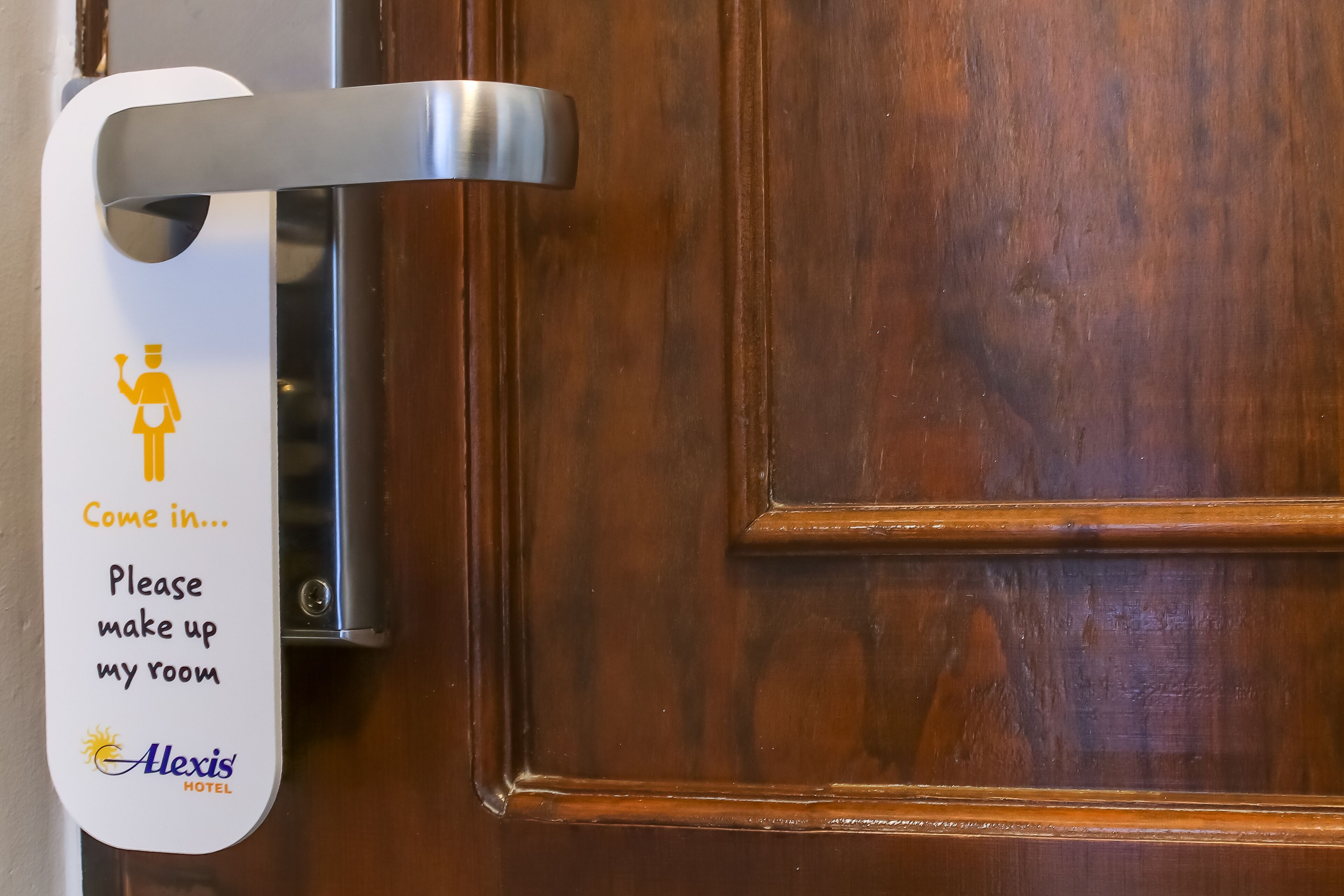 A hotel room door handle with a sign that reads "Come in... Please make up my room" and the logo "Alexis Hotel".