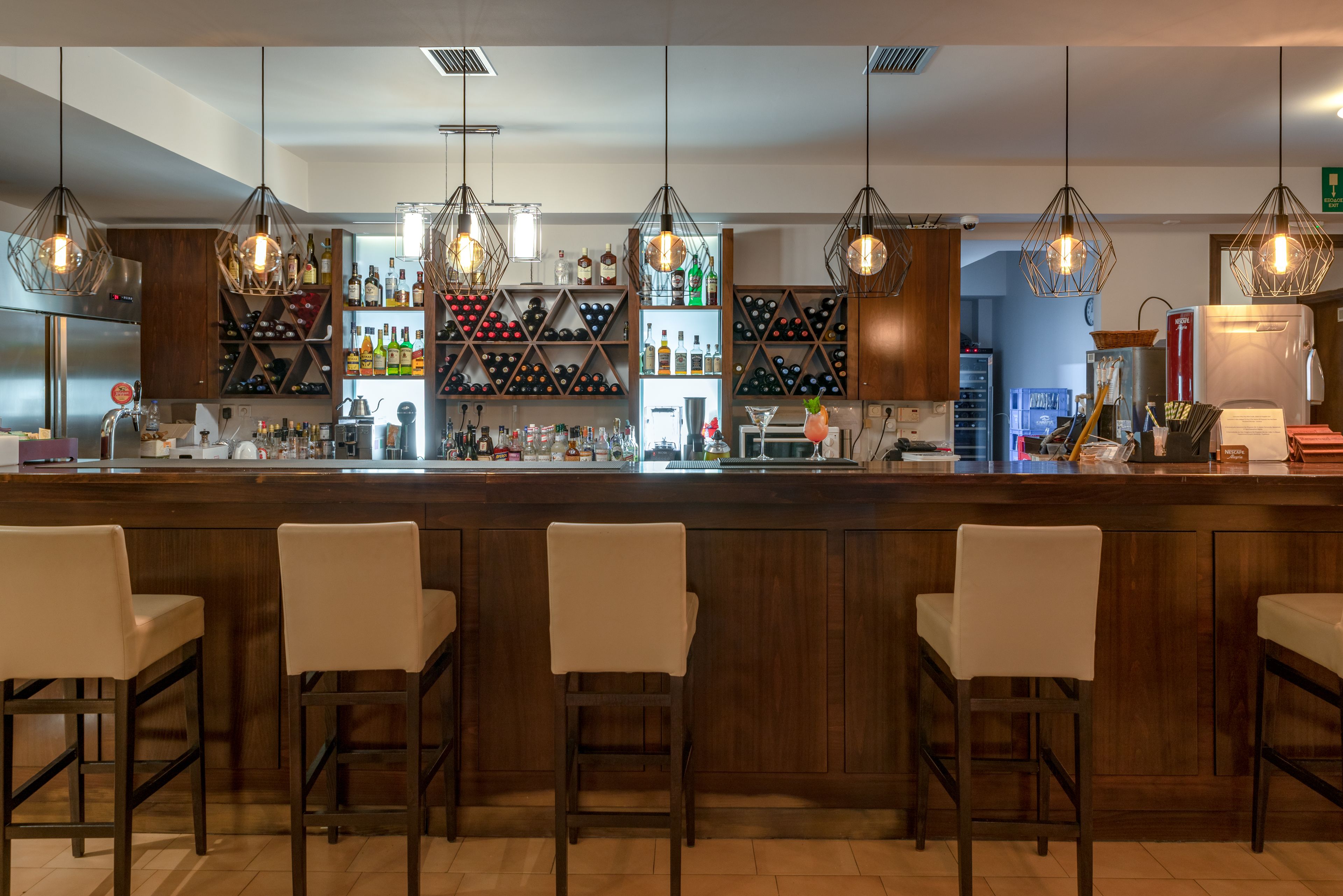 Un espace bar doté d’un comptoir en bois, de plusieurs étagères remplies de bouteilles et de luminaires suspendus.