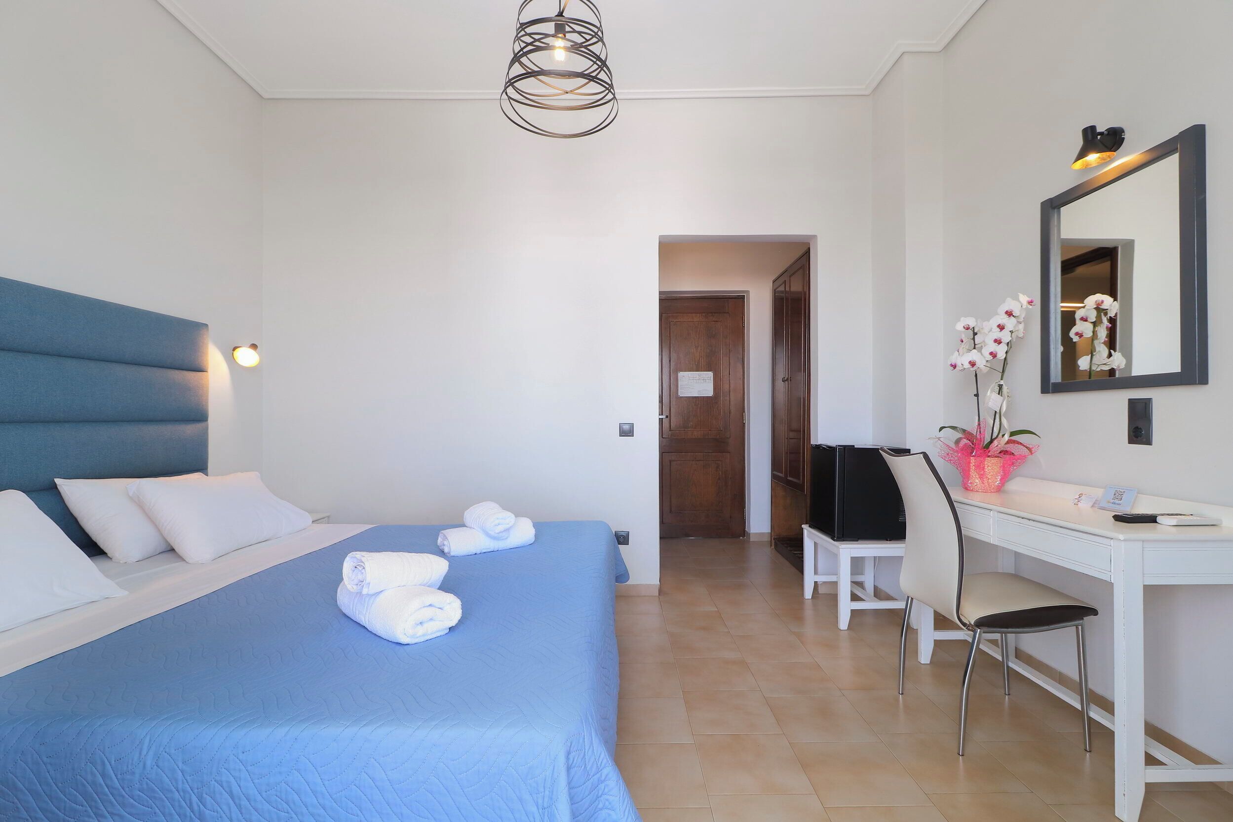 Une chambre d’hôtel comprenant un lit, un bureau, une chaise, un miroir et une porte donnant sur une autre pièce.