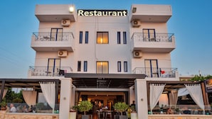 A two-story restaurant with a modern facade, outdoor seating area, and a stone wall entrance. - Alexis Hotel (Chania)