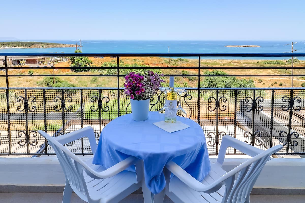 Un balcón con mesa y sillas, vista al mar y una barandilla.