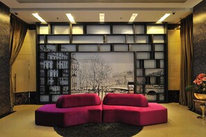 A modern living room with a large window displaying a cityscape, a red sofa, and a decorative wall panel.
