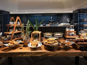 A buffet setup with various food items, a coffee station, and a kitchen area in the background. - Mövenpick Hotel Windhoek (Windhoek)
