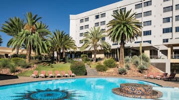 A hotel with a swimming pool, palm trees, and a modern building.