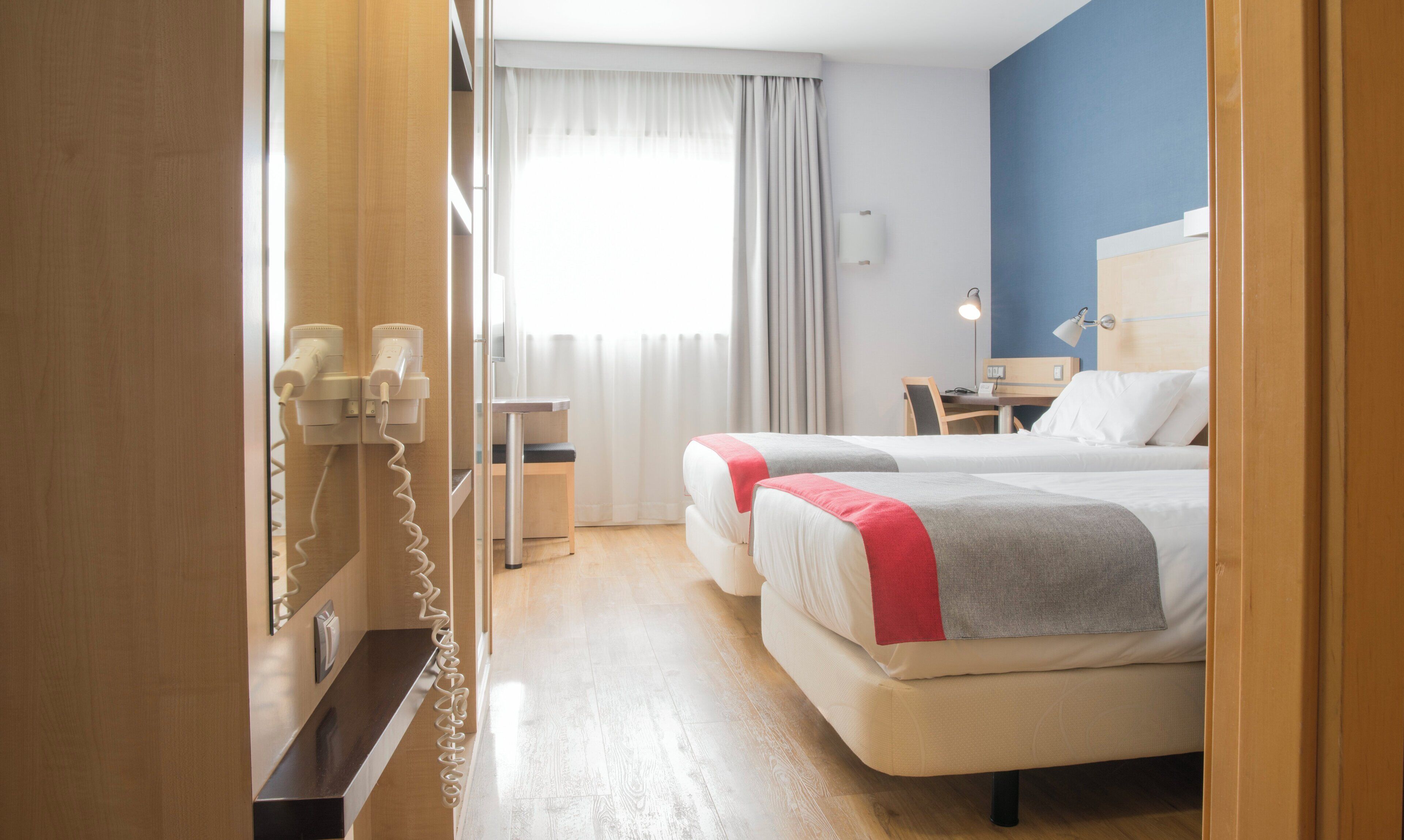 A hotel room with two beds, a desk, a chair, a telephone, and a window with curtains.